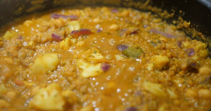 Close up shot of Indian dal (lentil) curry been cooked with cauliflower, chickpeas, onions and red lentils along with masala and turmaric in the kitchen.