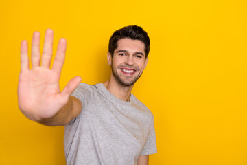 Portrait of attractive cheerful brown haired guy giving high five isolated over bright yellow color...
