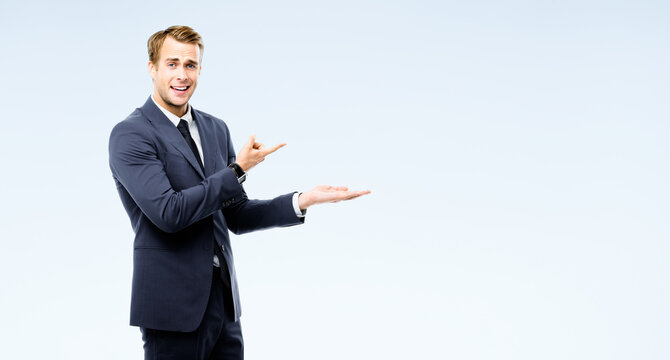 Excited businessman in suit showing, holding, giving some product or copy space for advertising text, isolated on grey background. Young happy corporate business man at studio image. Professional.