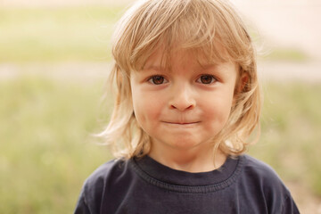 close-up portrait of the pensive face of a little blond boy on a green background summer street