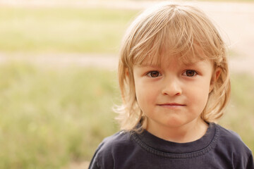 close-up portrait of the pensive face of a little blond boy on a green background summer street