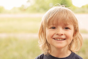 close-up portrait of the happy face of a little blond boy on a green background summer street