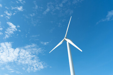 Fototapeta premium wind mill or also wind-turbine on wind farm in rotation to generate electricity energy on outdoor with sun and blue sky; conservation and sustainable energy concept.