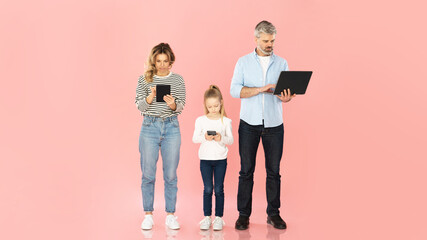 Family Browsing Internet Using Computers And Phone On Pink Background