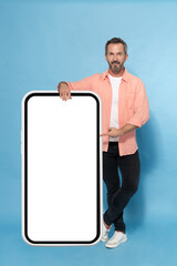 Middle aged grey haired man leaned on huge, giant smartphone pointing on white screen happy smiling...