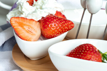 Dessert of fresh strawberries and whipped cream in small white bowls on a wooden stand. White chinaware. beautiful kitchen utensils