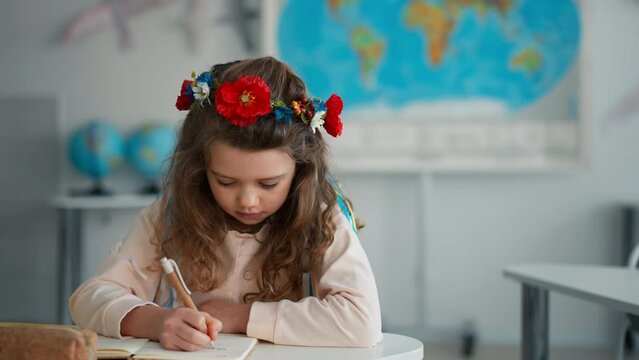 Little sad Ukrainian girl sitting in classroom during class, concept of enrolling Ukrainian kids to schools.