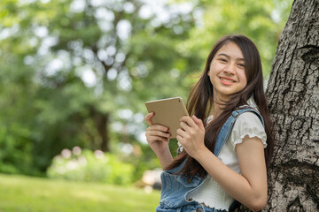 Thoughtful smile woman in park using smart digital tablet, Portrait of a young charming business woman checking online Business work on her smart tablet or labtop  outdoors in the park on soft green 