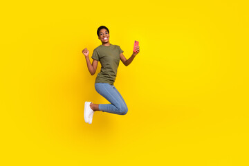 Fototapeta na wymiar Full body portrait of successful funky person jump hold telephone raise fist isolated on yellow color background