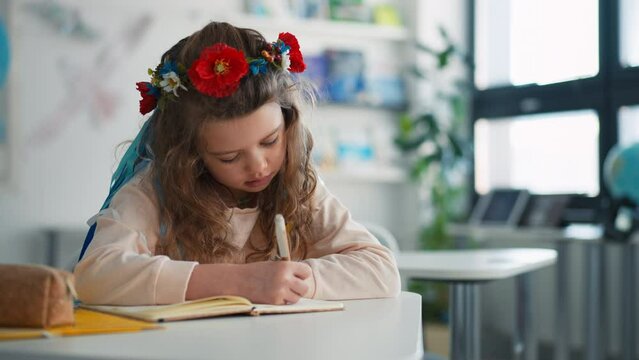 Little sad Ukrainian girl sitting in classroom during class, concept of enrolling Ukrainian kids to schools.