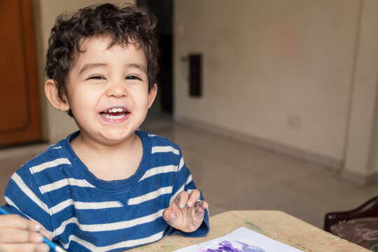 child painting with paints and colored pencil laughing making a drawing