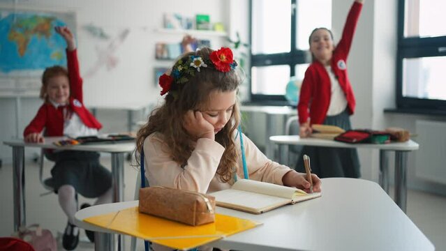 Little sad Ukrainian girl writing in classroom during class, concept of enrolling Ukrainian kids to schools.