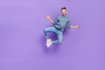 Photo of funny childish guy dressed grey shirt jumping high empty space isolated purple color background