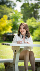 Beautiful young woman girl in beige shirt posing in Green city Park background , Smile girl Listening Music with Headphones feeling Touching Happiness. People lifestyle concept. Mock up copy space