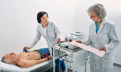 Cardiogram test. Elderly male patient receives heart rate monitored using electrocardiogram equipment with two doctors cardiologist