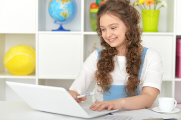 Cute schoolgirl doing home work with  laptop in the room