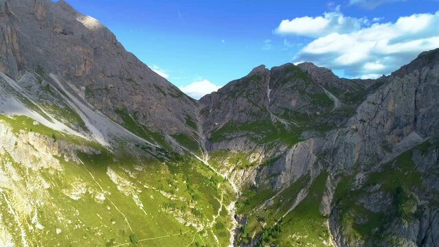 Rising aerial view up grass covered slope passage from base of South Tyrol Plose Peitlerkofel breath taking mountain valley