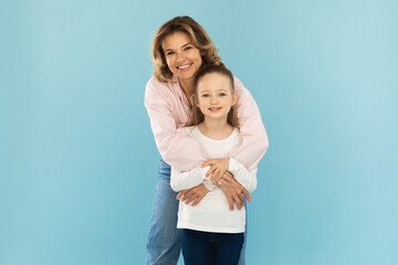 Joyful Mom Embracing Little Daughter Standing Over Blue Background