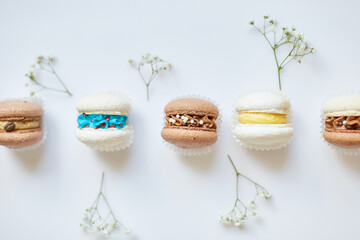 Top view set of different french cookies macaroons, cake macarons with flowers on white background, colorful almond cookies, pastel colors.