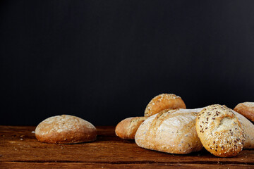 Assorted different types of bread on a wooden table on a black background.