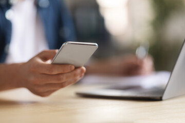 Young Male Using Modern Smartphone While Sitting At Desk With Laptop
