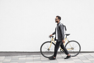 Young handsome man with bike over white wall background in city, Smiling student man with bicycle...