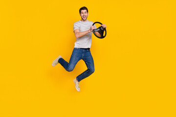 Fototapeta na wymiar Full size photo of nice brunet millennial guy jump drive wear t-shirt jeans sneakers isolated on yellow background