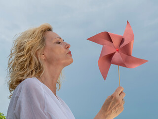 A blonde woman plays with a red pinwheel by blowing to make it spin