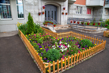 Fototapeta na wymiar Flowerbed and planters of bright flowers and various plants in front of the entrance of a residential building. Agriculture Landscaping landscaping of cities.