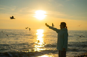 Fototapeta premium Caucasian woman feeding seagulls on the sea at sunset. 