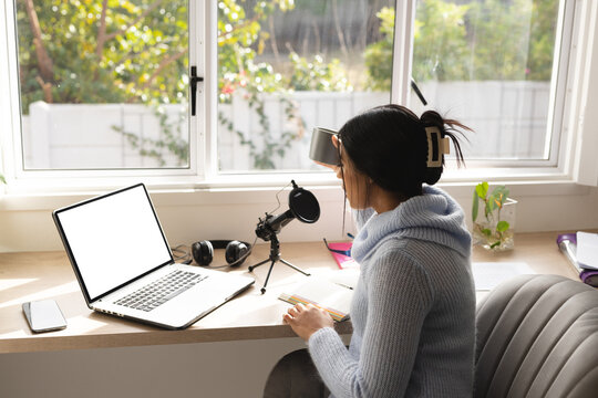Biracial young woman recording podcast through microphone over laptop at home studio
