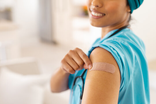 Midsection of smiling biracial young female doctor showing bandage on arm at clinic