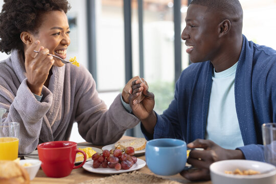 Romantic african american mid adult couple holding hands while having breakfast at dining table