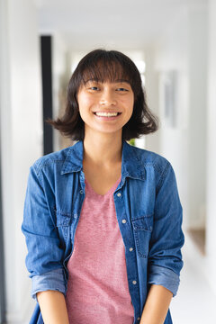 Portrait of smiling asian young woman with short hair wearing denim jacket standing at home