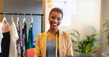 Portrait of smiling african american young female fashion designer with tape measure in studio