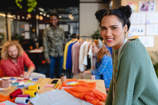 Portrait Of Smiling Caucasian Female Fashion Designer With Colleagues In Background At Office