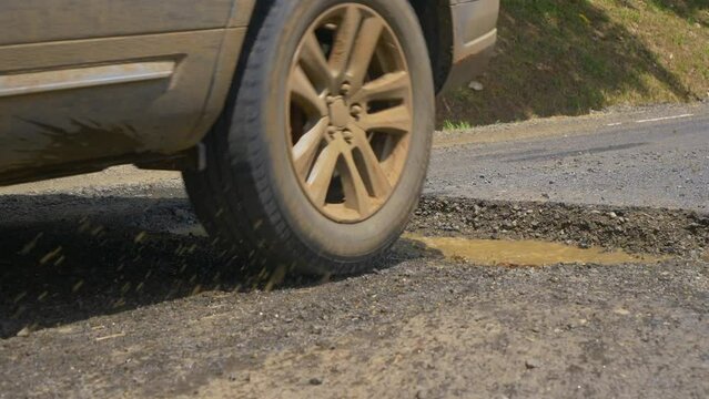 SLOW MOTION, CLOSE UP, DOF: Murky water splashes as car drives into a big hole in pavement. Tourist SUV drives into a massive pothole gaping in the middle of a country road in scenic central Panama.