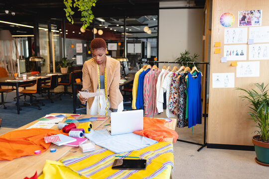 African american female fashion designer reading document at desk in studio
