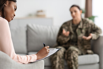 Black Female Psychologist Taking Notes During Therapy Session With Military Woman