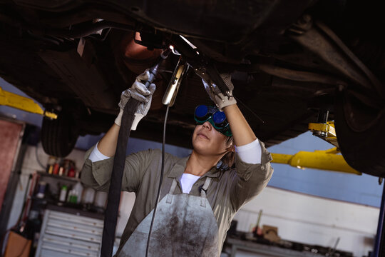 Mid adult asian female welder welding while repairing car under car lift in workshop