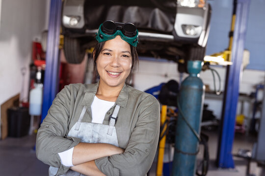 Portrait of smiling mid adult asian female welder with arms crossed standing in workshop