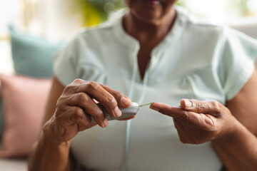 Midsection of african american senior woman examining sugar with glucometer while sitting on sofa