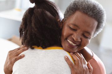 Close-up of smiling african american senior woman embracing young daughter at home