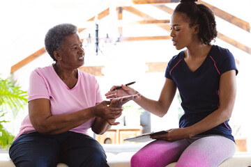 African american senior woman showing hand to female physiotherapist while sitting on table at home