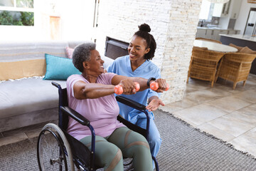 African american doctor guiding senior woman exercising with dumbbells while sitting on wheelchair