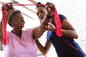 African american female physiotherapist assisting senior woman in exercising with resistance band