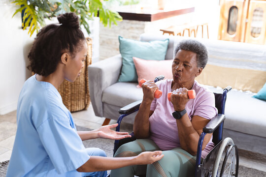 African american female doctor instructing senior woman exercising with dumbbells on wheelchair