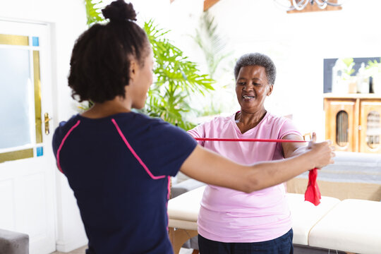 African american female physiotherapist helping senior woman in exercising with resistance band