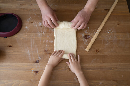 Hands Of Father And Daughter Rolling Dough On Table