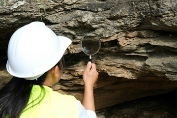 Asian female geologist researcher analyzing rocks with a magnifying glass in a natural park....